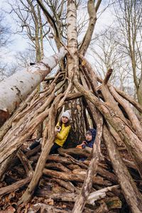 zwei Kinder sitzen in einer selbstgebauten Stockhütte im Wald